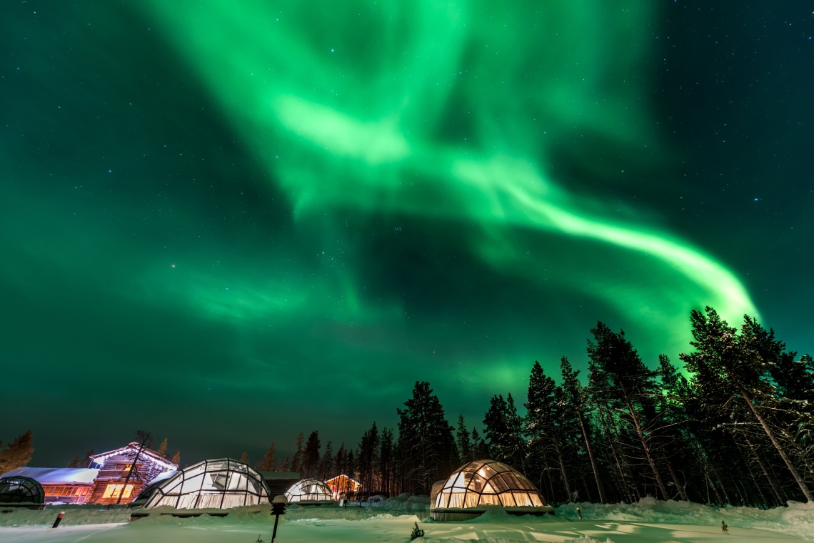 Bright aurora above glass igloo in Finland